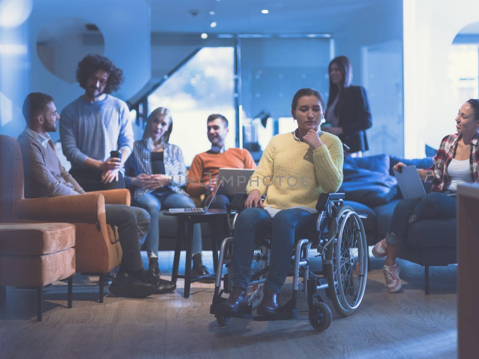 Portrait of disabled businesswoman in a wheelchair in front of her diverse business team in a modern open space coworking office space. High quality photo