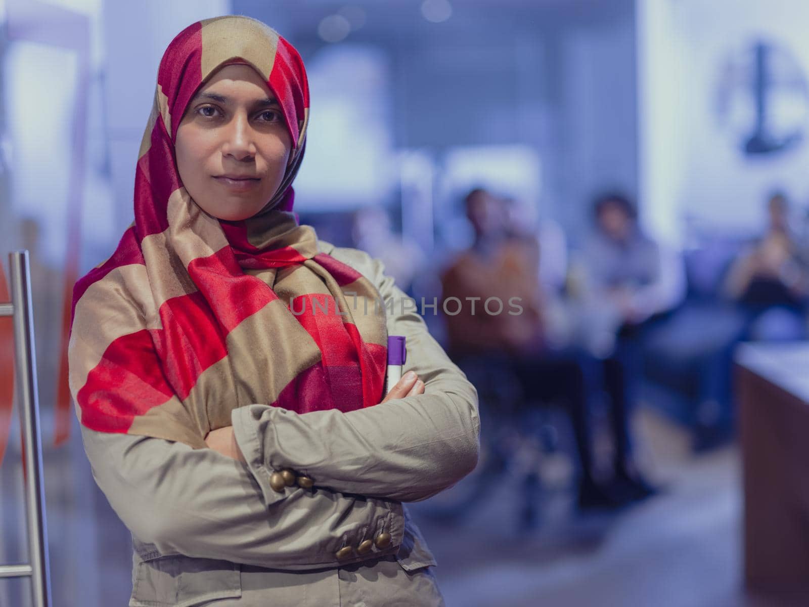 Portrait of Muslim woman wearing hijab in a modern open space coworking office. Middle eastern Successful Arab businesswoman in creative startup office. Disabled businessman in a wheelchair on team meeting in background.