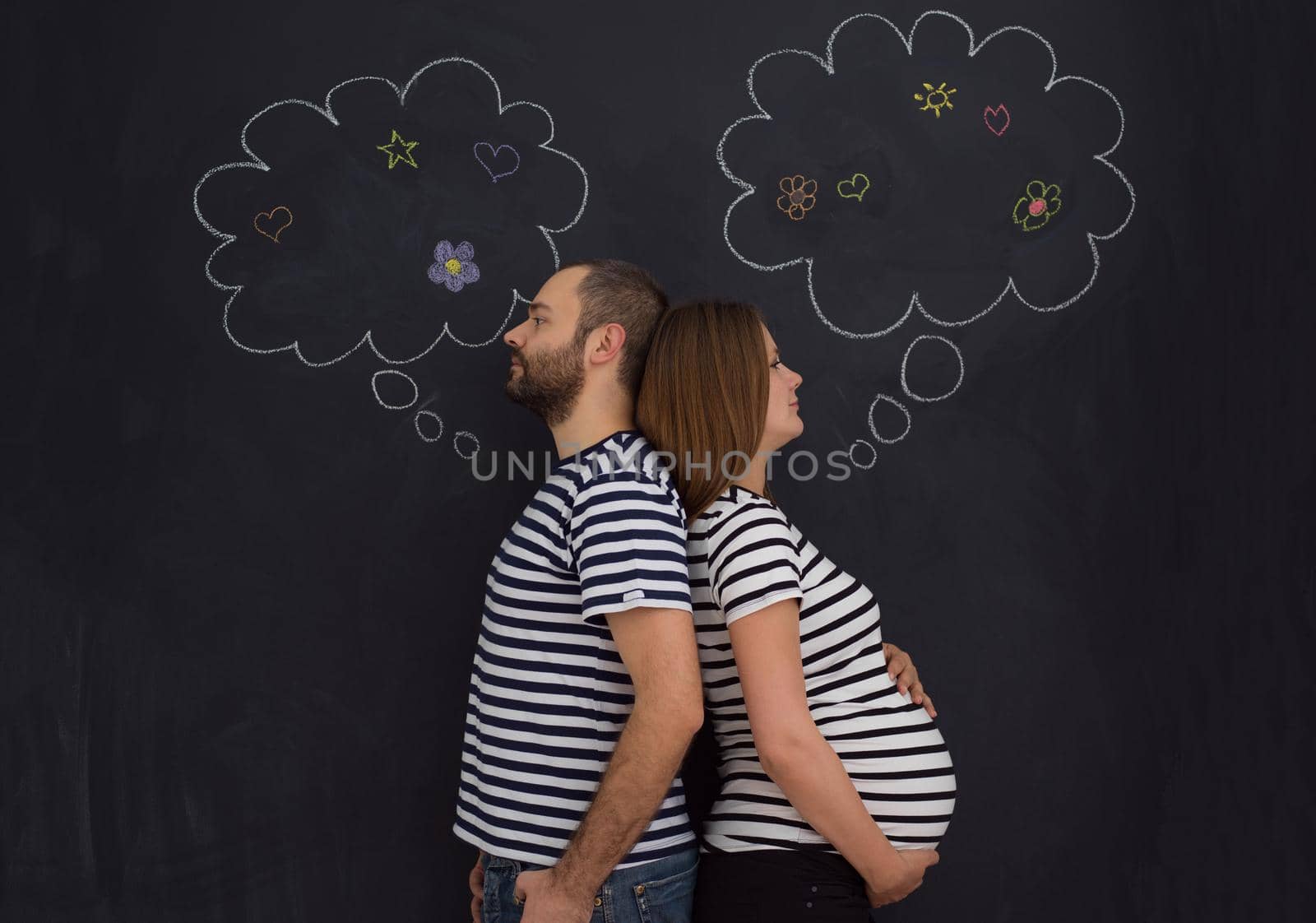 pregnant couple posing against black chalk drawing board by dotshock