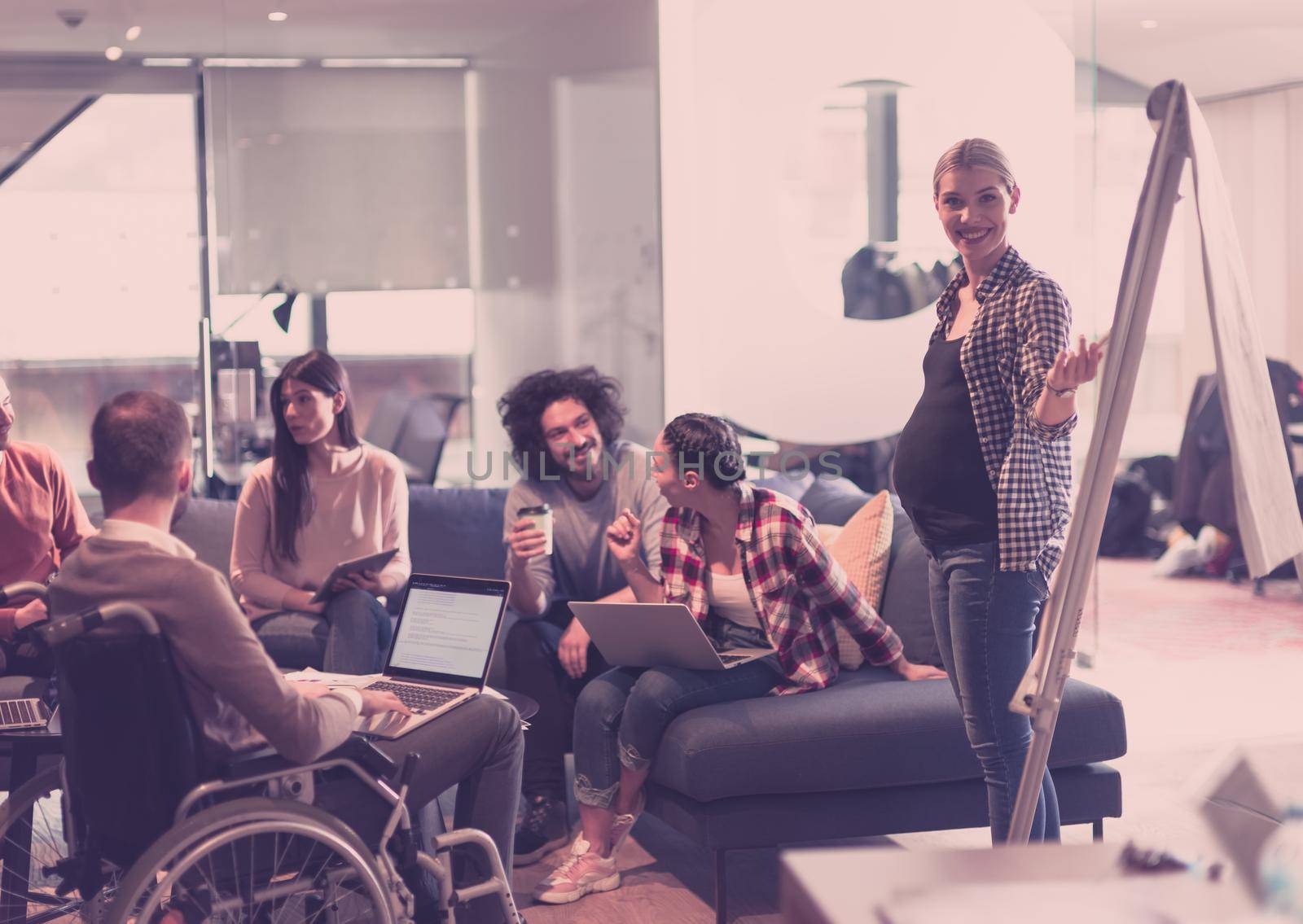 Pregnant Businesswoman Leads Creative Meeting Of Diverse Business Team In Modern Coworking Open Space Office, Disabled coworker in wheelchair attending training 