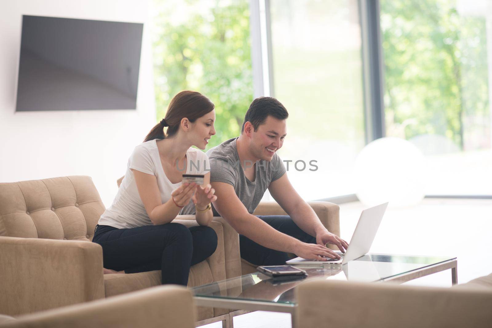 happy young couple buying online using laptop a computer and a credit card in their luxury home villa