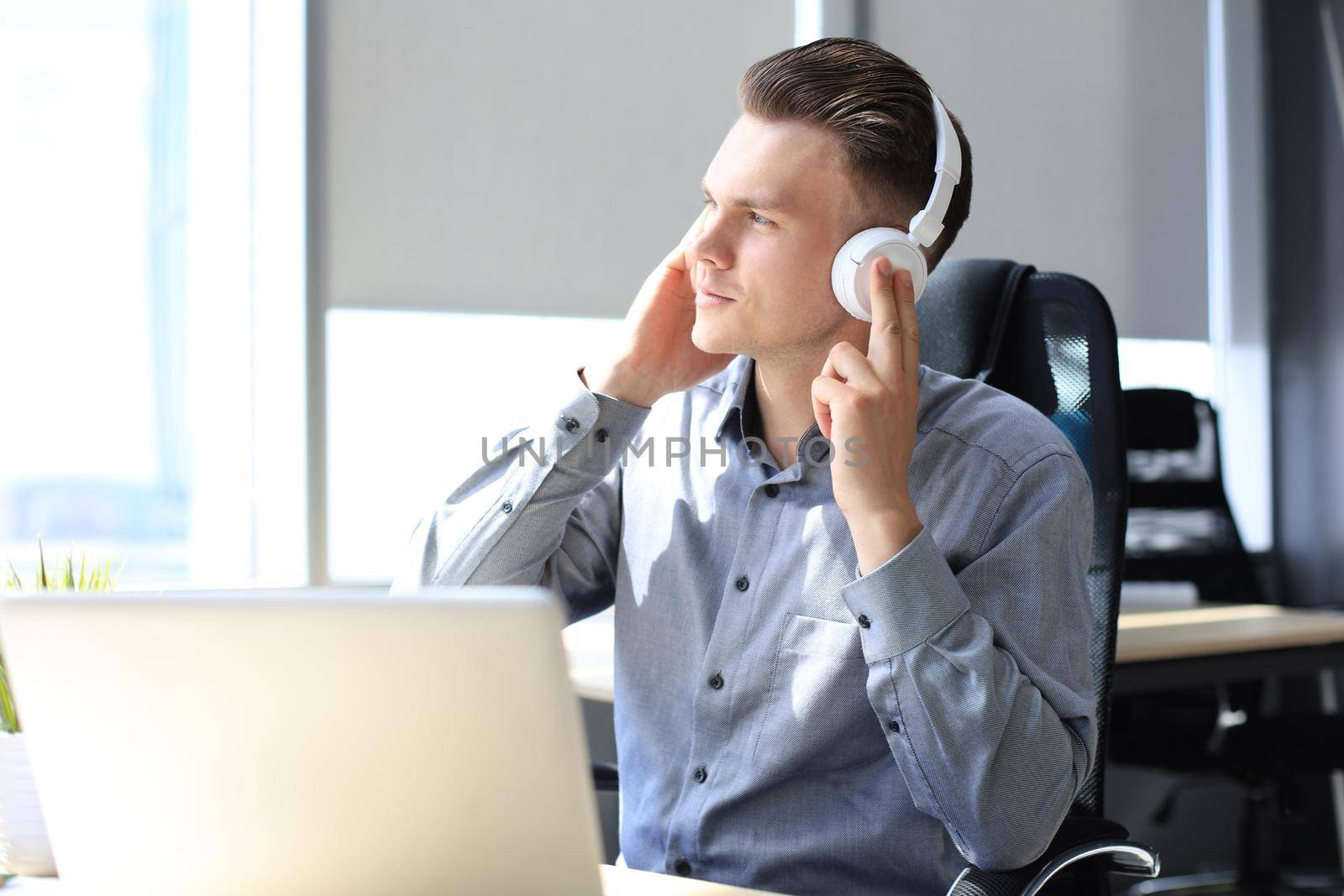 Smiling handsome businessman relaxing and listening music in earphones in a modern office.