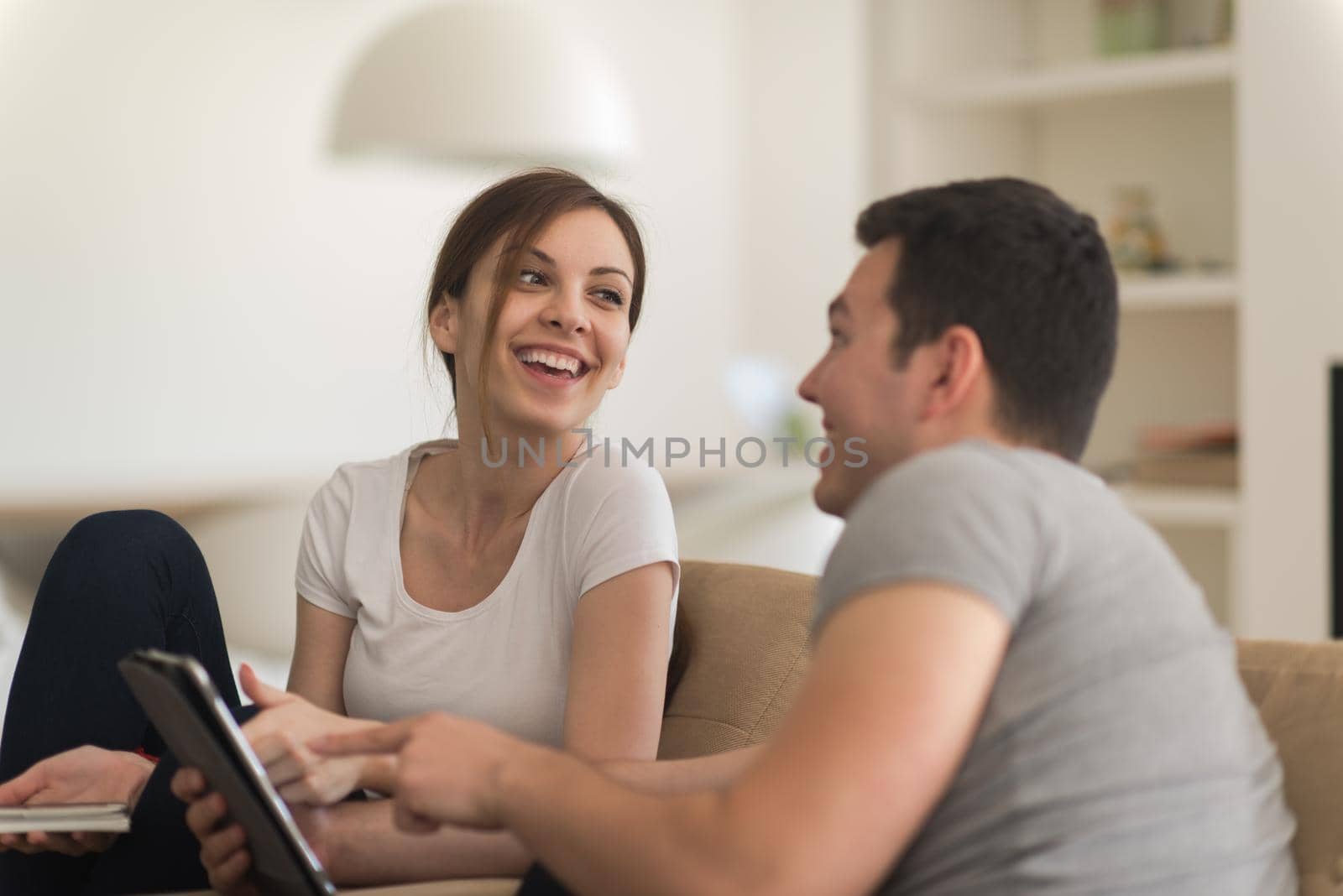 Young couple relaxing at luxurious home with tablet computers reading in the living room on the sofa couch.