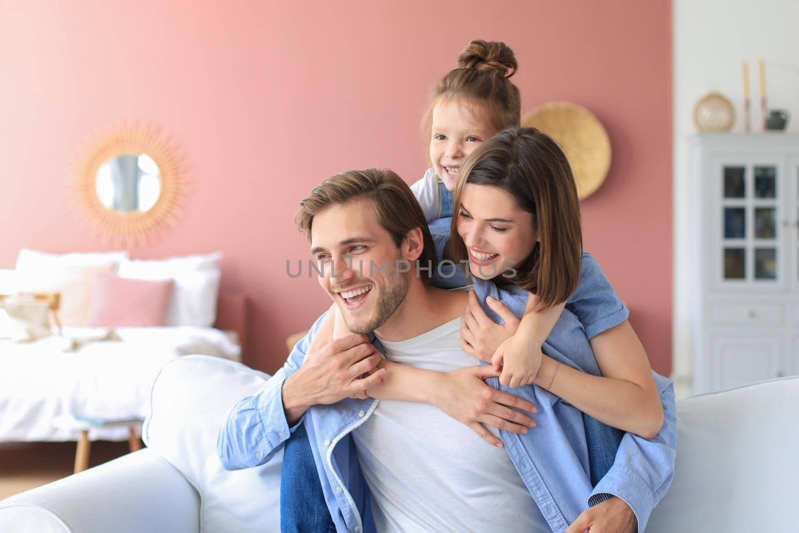 Young Caucasian family with small daughter pose relax on sofa in living room, smiling little girl kid hug embrace parents, show love and gratitude, rest at home together