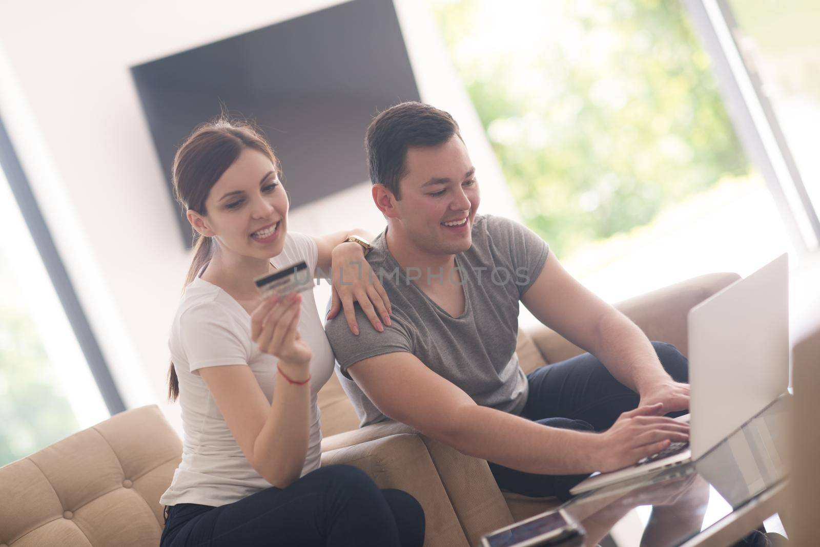 happy young couple buying online using laptop a computer and a credit card in their luxury home villa