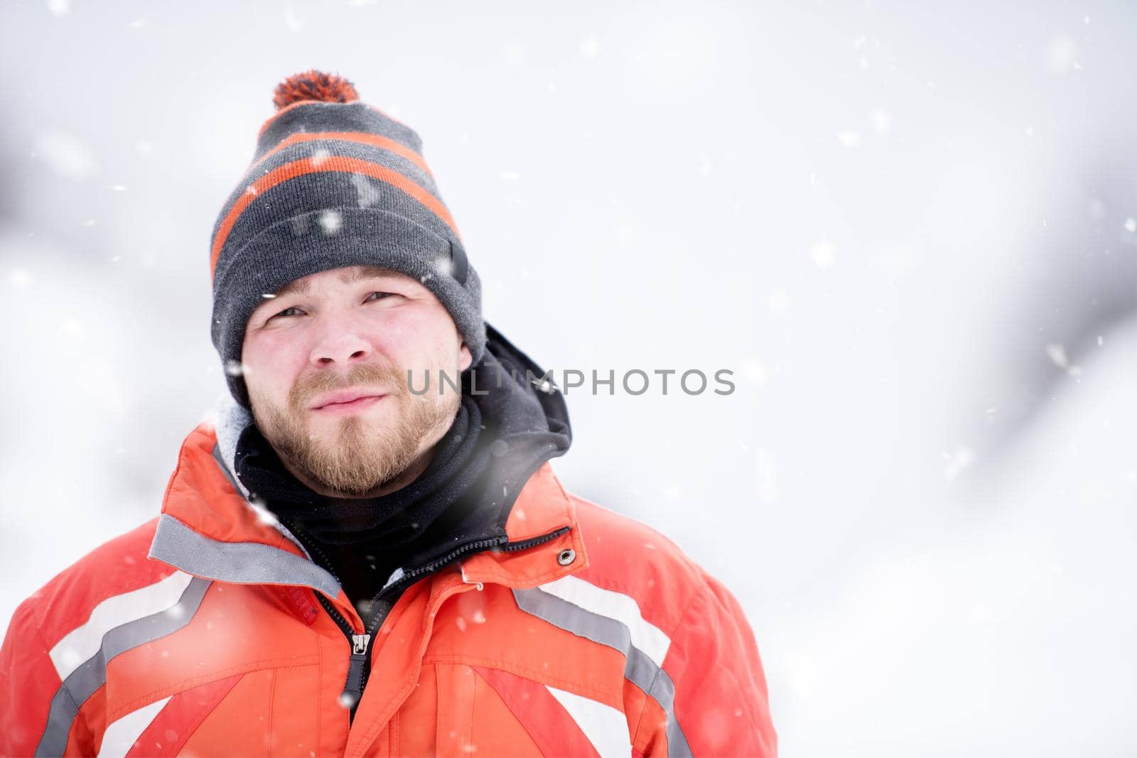 Man in winter season  Portrait of young man in warm clothes enjoying snowy day with snowflakes around him in the winter forest