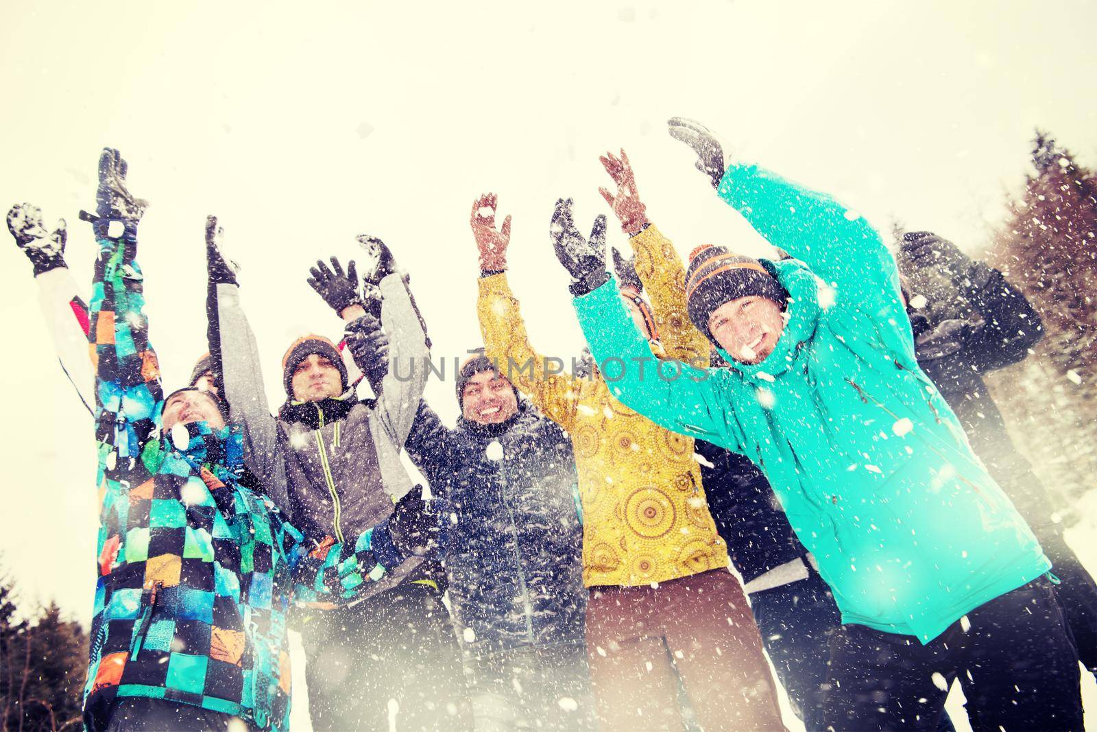 group of young happy business people having fun throwing snow in the air while enjoying snowy winter day with snowflakes around them during a team building in the mountain forest