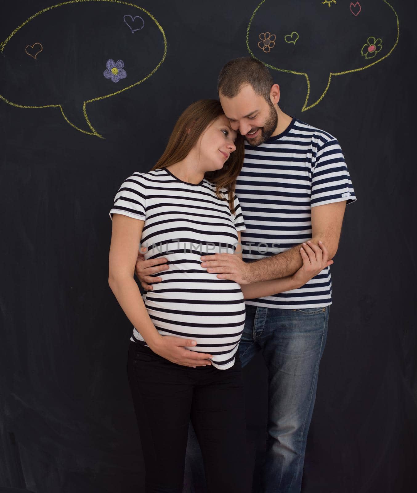pregnant couple posing against black chalk drawing board by dotshock