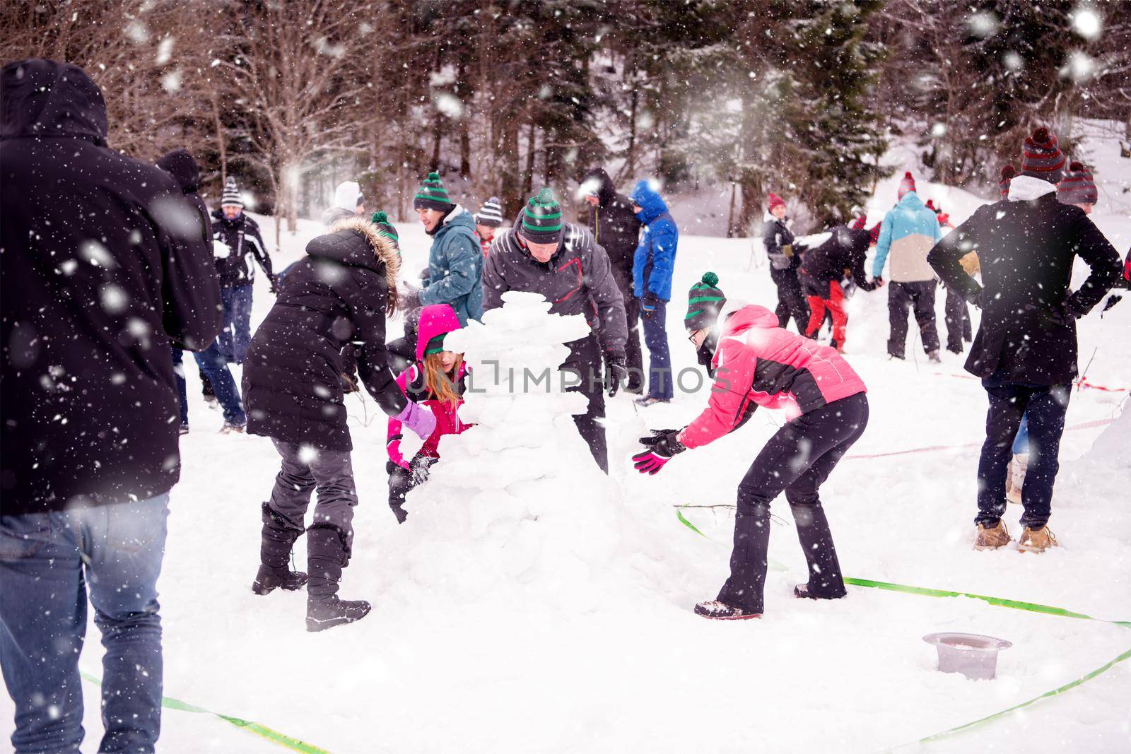 group of young happy business people having a competition in making snowmen while enjoying snowy winter day with snowflakes around them during a team building in the mountain forest