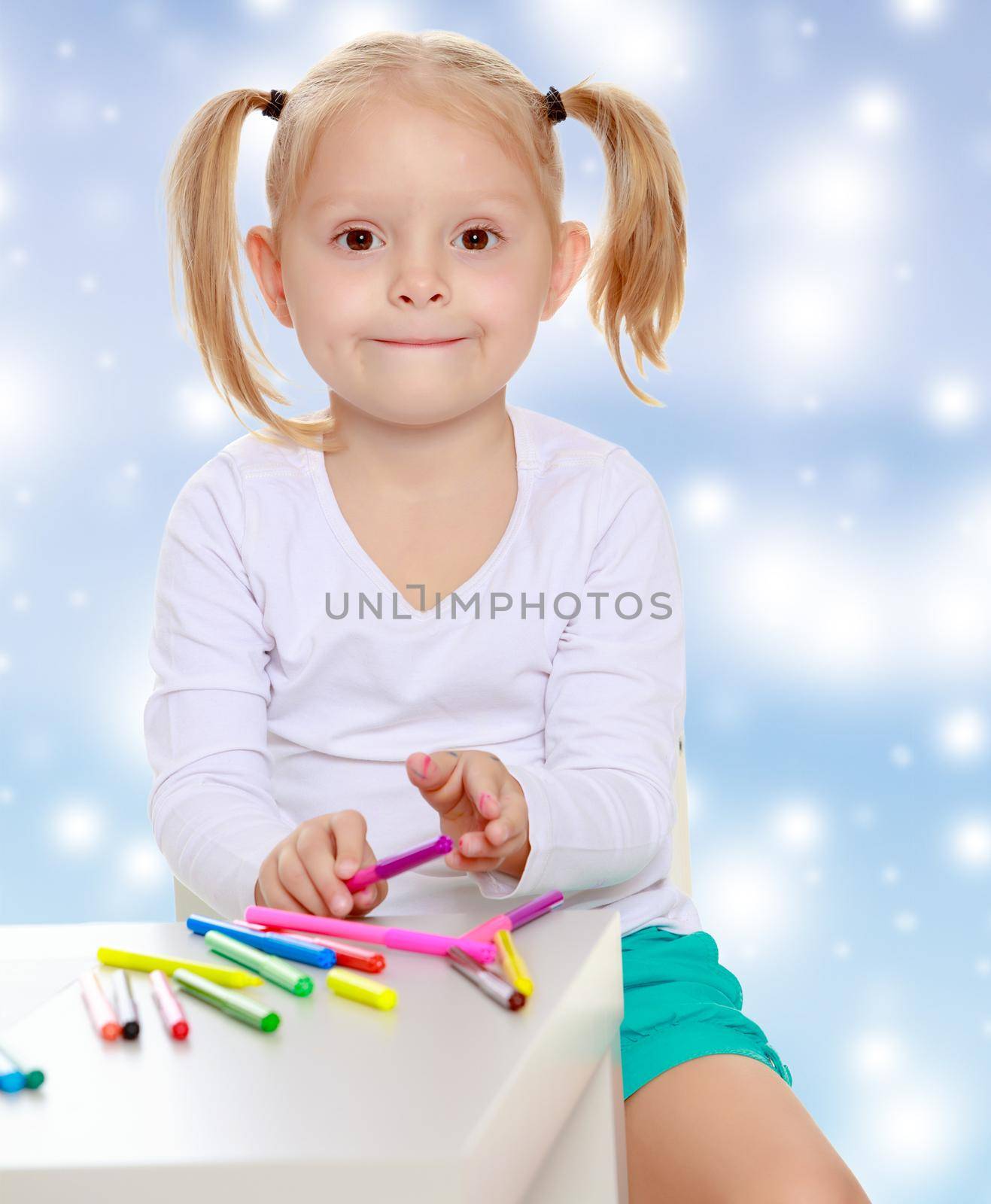 Pretty little blonde girl drawing with markers at the table.Girl holding in hands a pink marker.The concept of celebrating the New year, Holy Christmas, or child's birthday on a blue