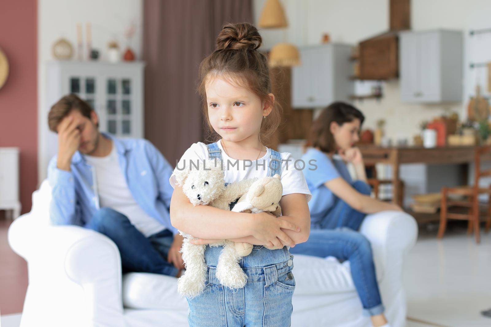 Young scolded parents sitting opposite each other on couch while little defenseless daughter upset looking at camera