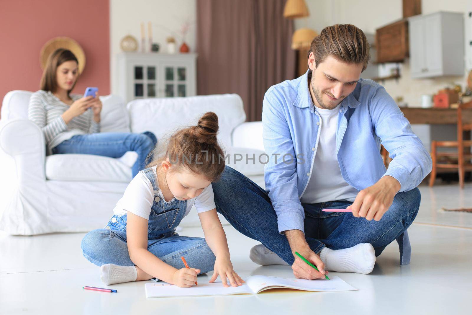 Happy father smilling daughter lying on warm floor enjoying creative activity, drawing pencils coloring pictures in albums, mother resting on couch, family spend free time together