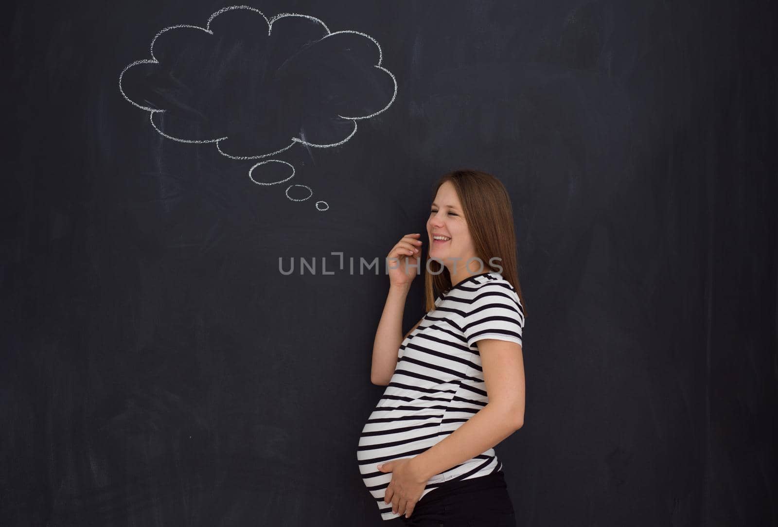 young pregnant woman thinking about names for her unborn baby to writing them on a black chalkboard