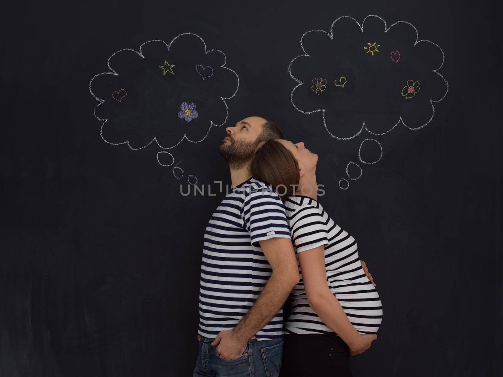 portrait of husband and pregnant wife posing against black chalk drawing board