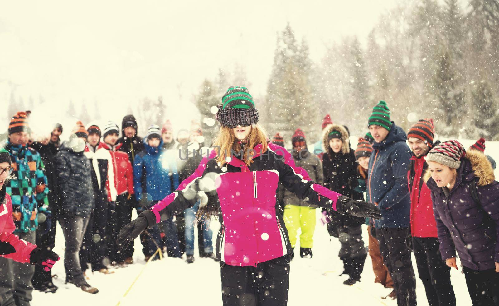 group of young happy business people having a Blindfolded games competition while enjoying snowy winter day with snowflakes around them during a team building in the mountain forest