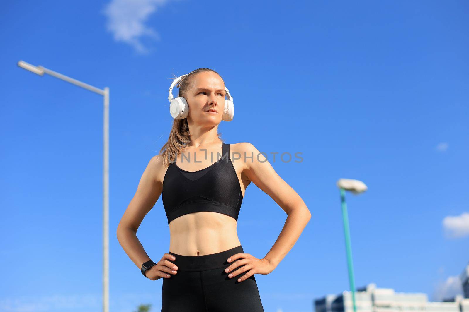 Beautiful woman in sports clothing and earphones looking aside from camera