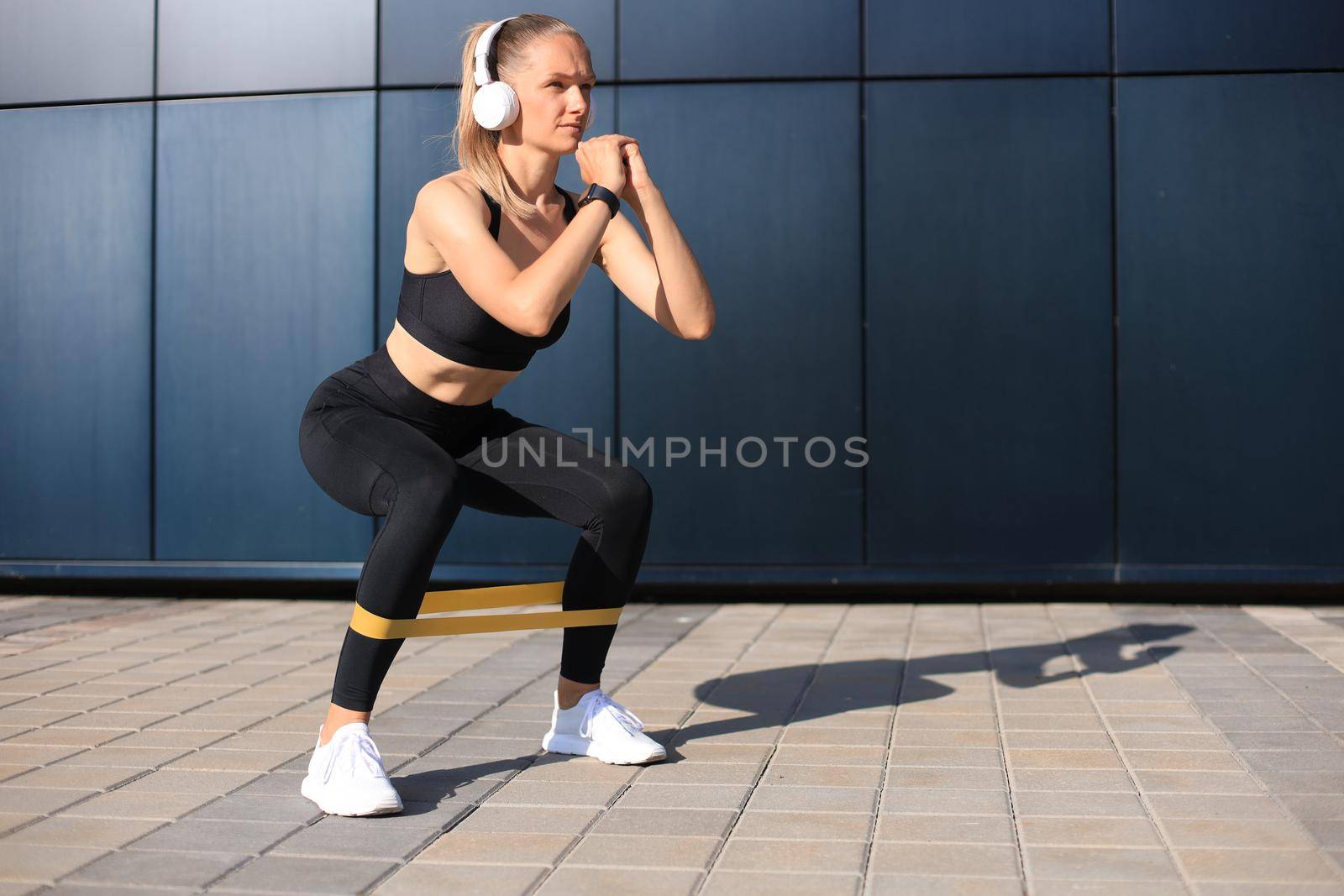 Sporty woman doing squats with fitness gum expander outdoors. by tsyhun