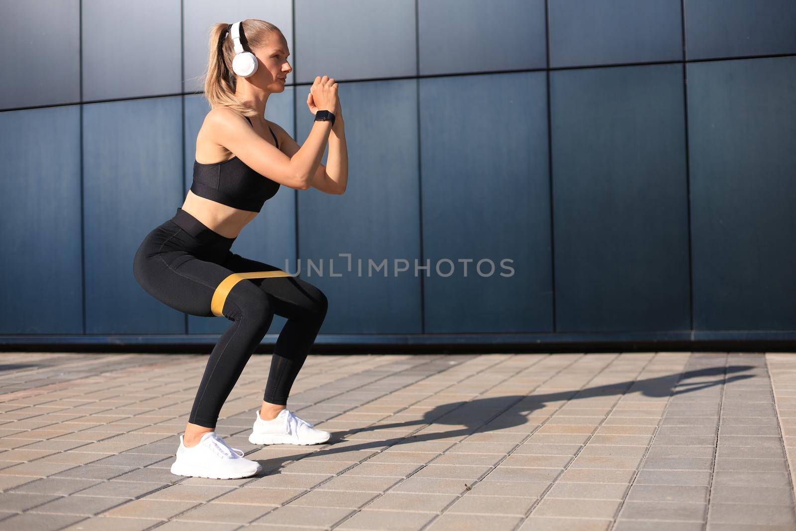 Sporty woman doing squats with fitness gum expander outdoors