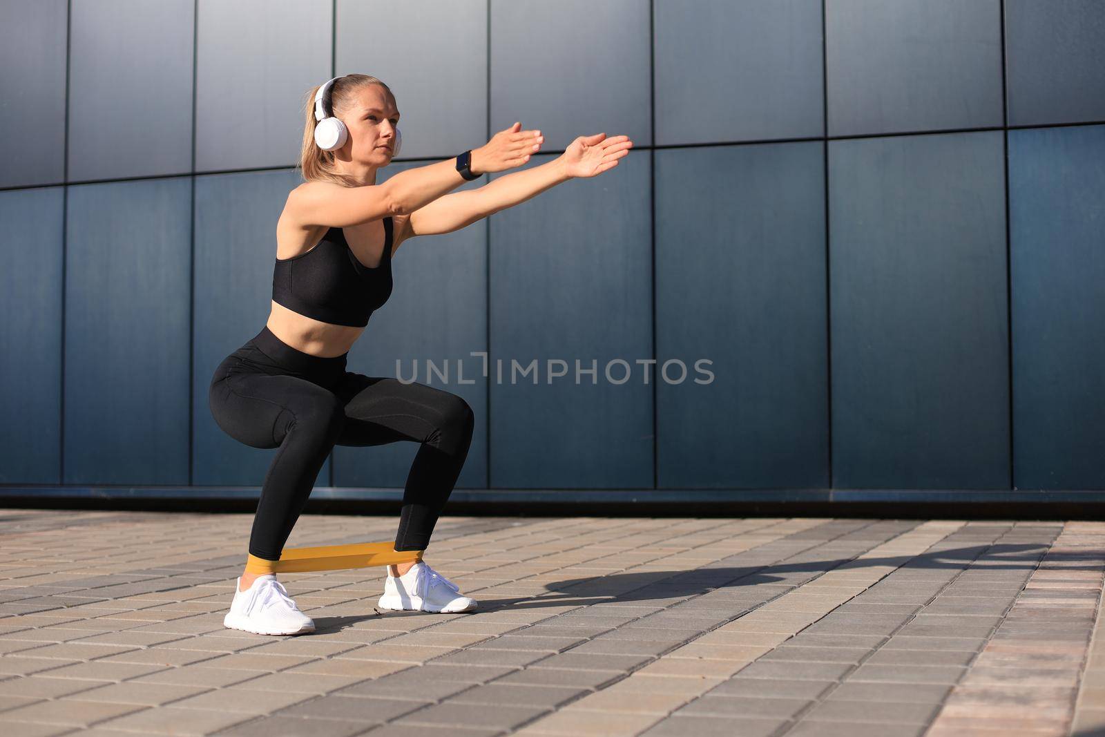 Sporty woman doing squats with fitness gum expander outdoors