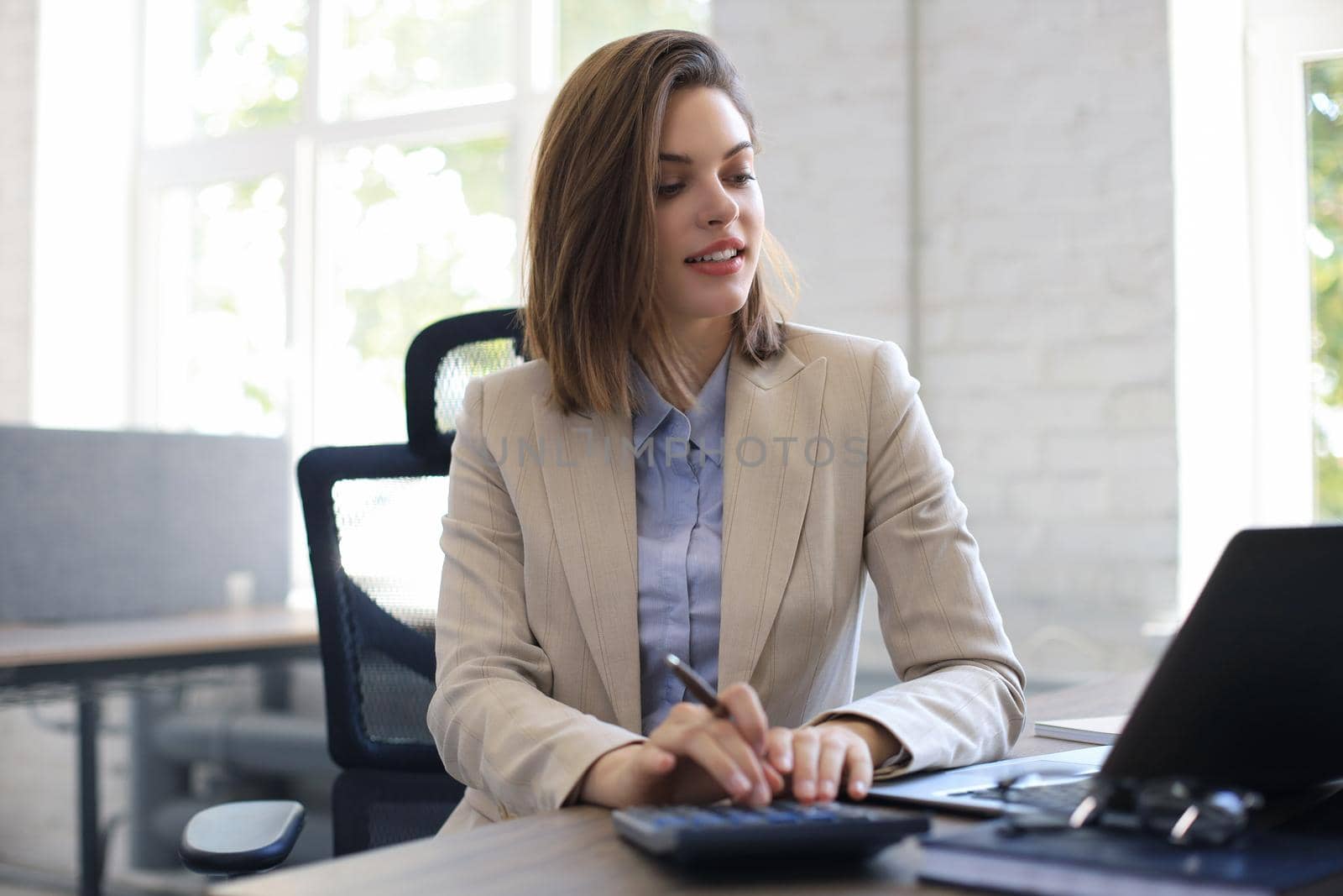 Attractive cheerful business woman working on laptop at modern office