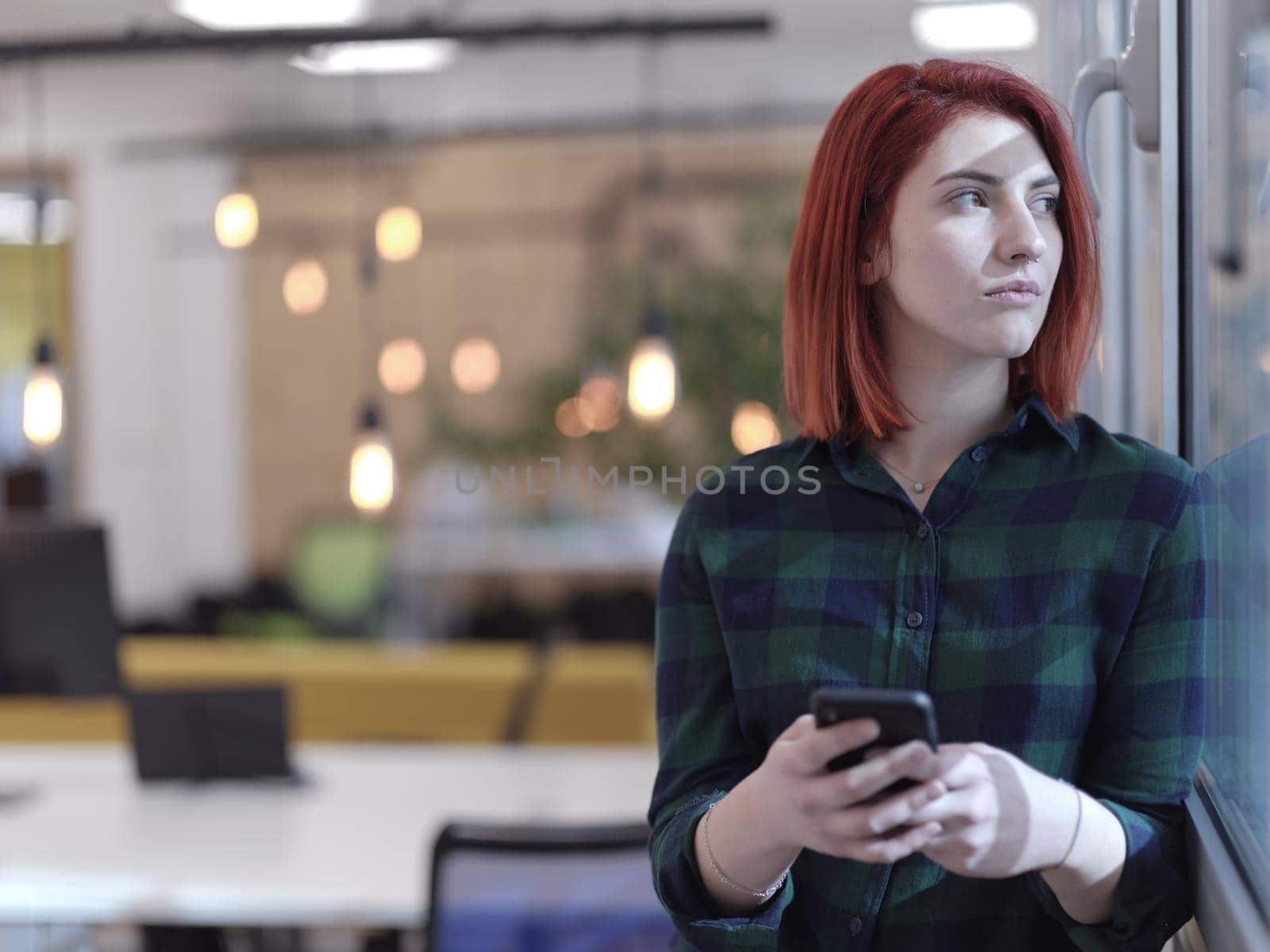 redhead business woman as influencer in creative modern coworking startup open space office using smart phone