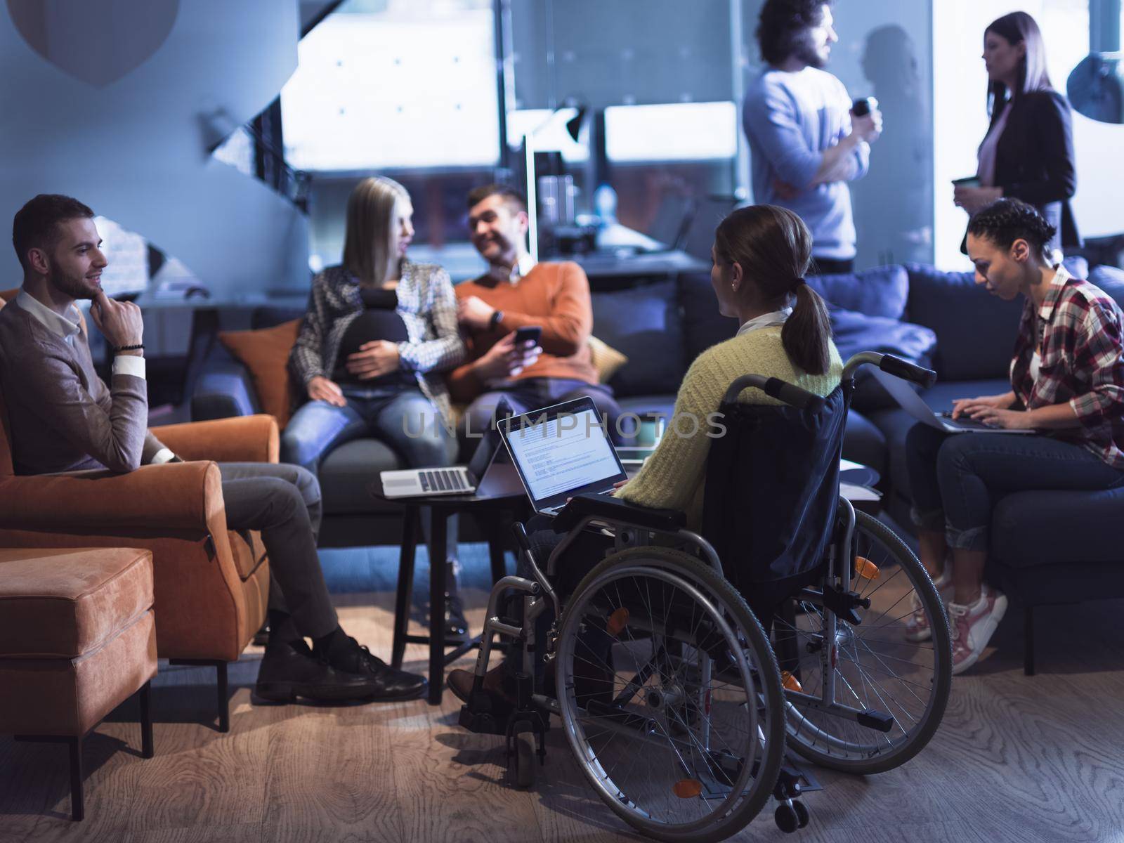 Closeup of a woman in a wheelchair working on a laptop computer at the office. Concept inclusion of disabled people in business. Business team meeting in background. High quality photo