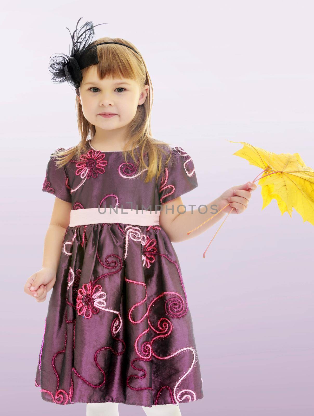 On a purple background, smooth transition from dark to light. Adorable little girl holding a maple leaf.