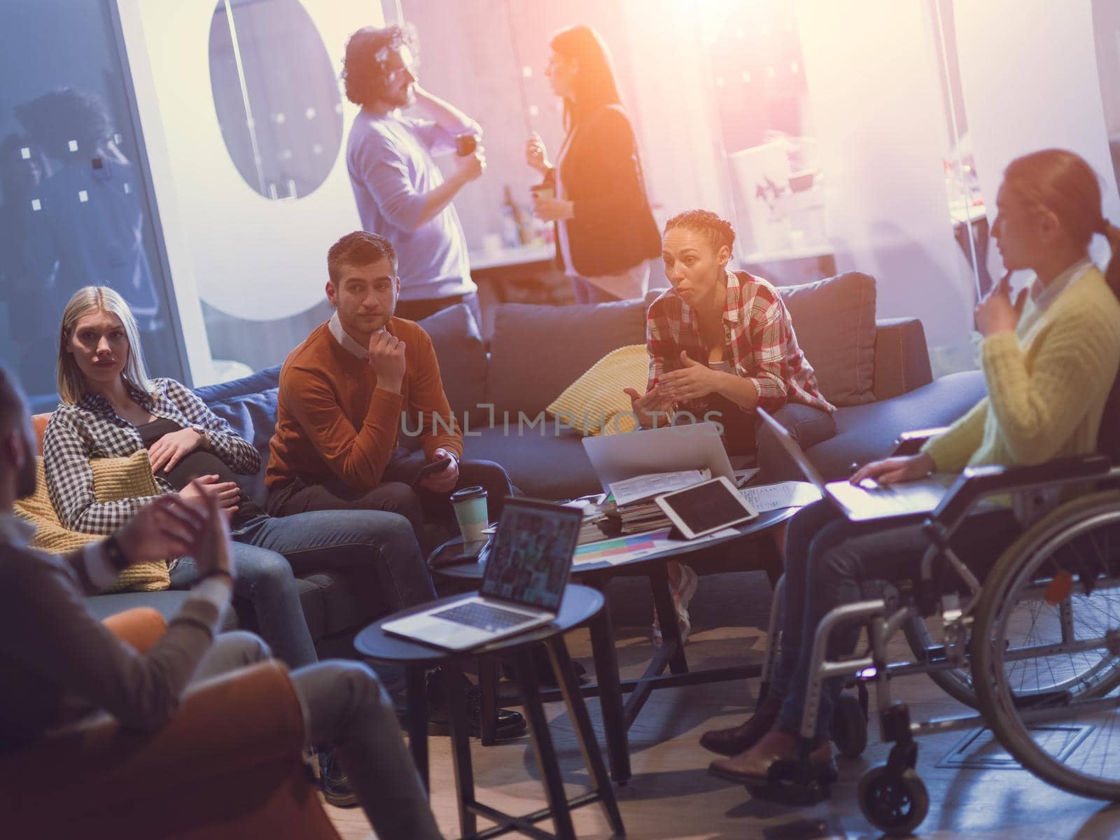 Handicapped businesswoman in a wheelchair on meeting with her diverse business team brainstorming about ideas and plans in a modern open space coworking office space. High quality photo