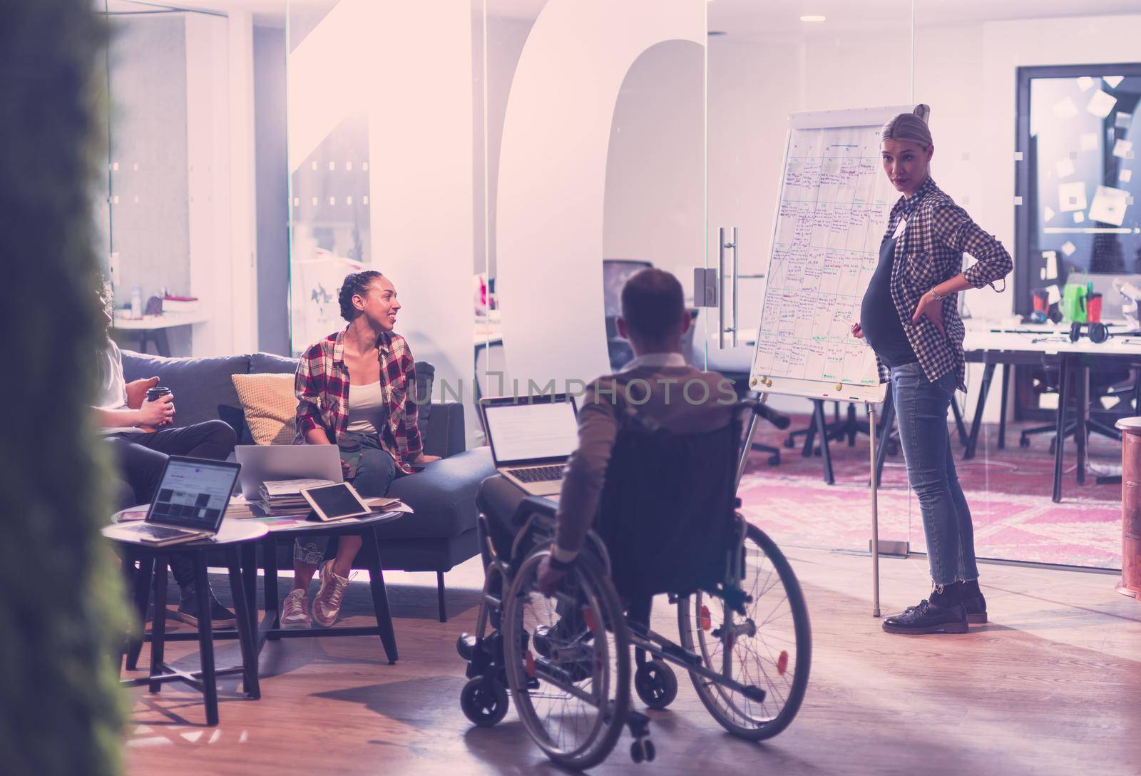 Pregnant Businesswoman Leads Creative Meeting Of Diverse Business Team In Modern Coworking Open Space Office, Disabled coworker in wheelchair attending training 