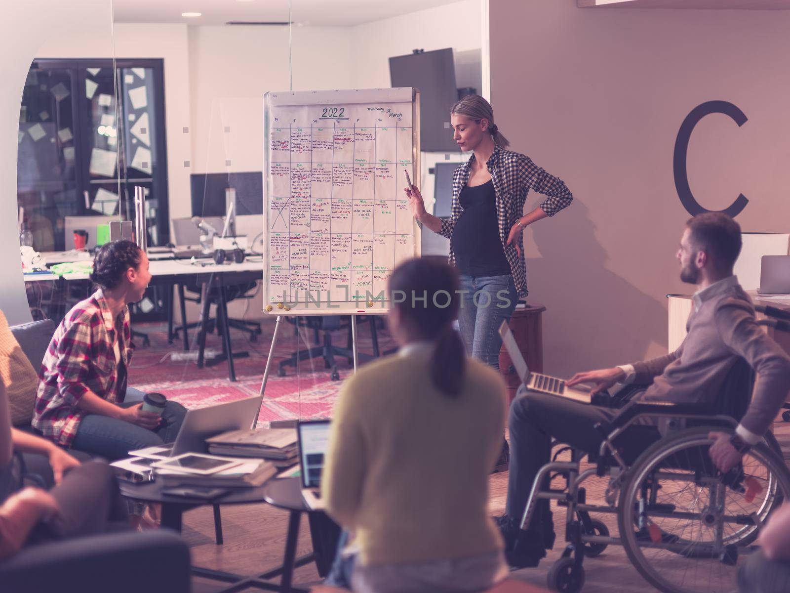 Pregnant Businesswoman Leads Creative Meeting Of Diverse Business Team In Modern Coworking Open Space Office, Disabled coworker in wheelchair attending training 