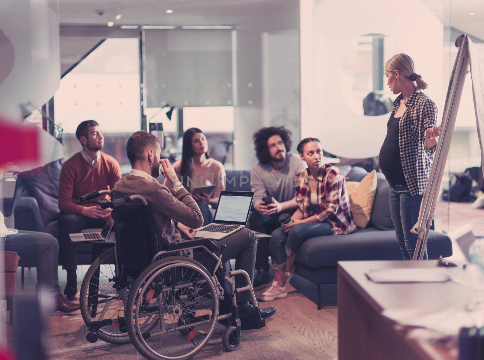Pregnant Businesswoman Leads Creative Meeting Of Diverse Business Team In Modern Coworking Open Space Office, Disabled coworker in wheelchair attending training 