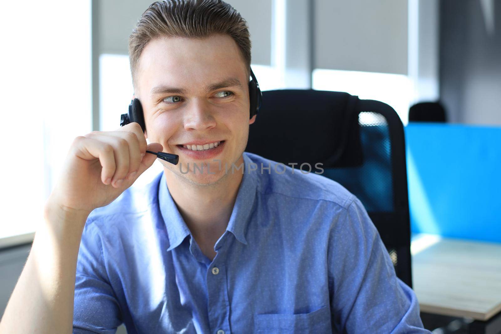 Cheerful young support phone male operator in headset, at workplace while using laptop, help service and client consulting call center concept. by tsyhun