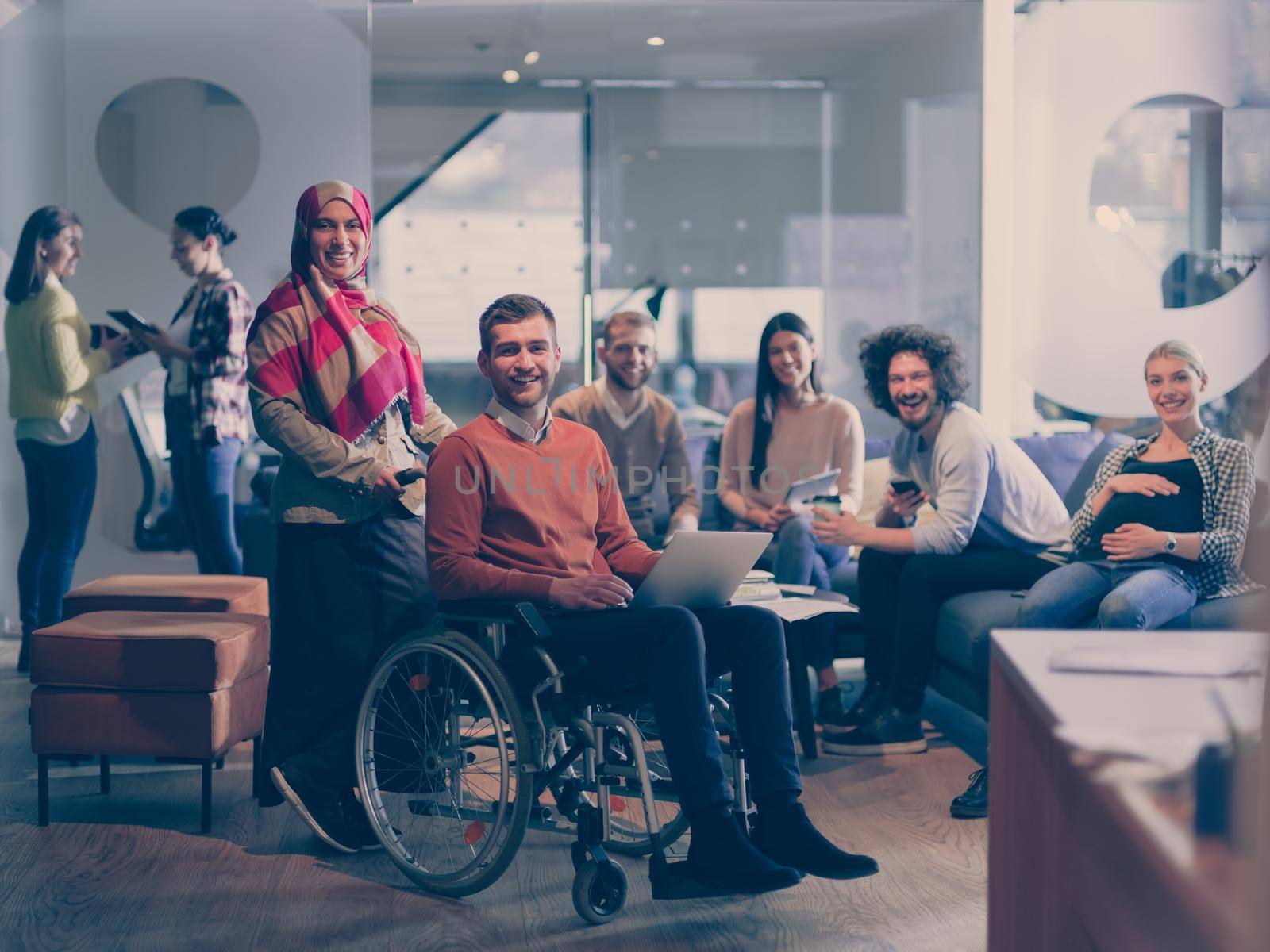Disabled businessman in a wheelchair at work in modern open space coworking office with team by dotshock