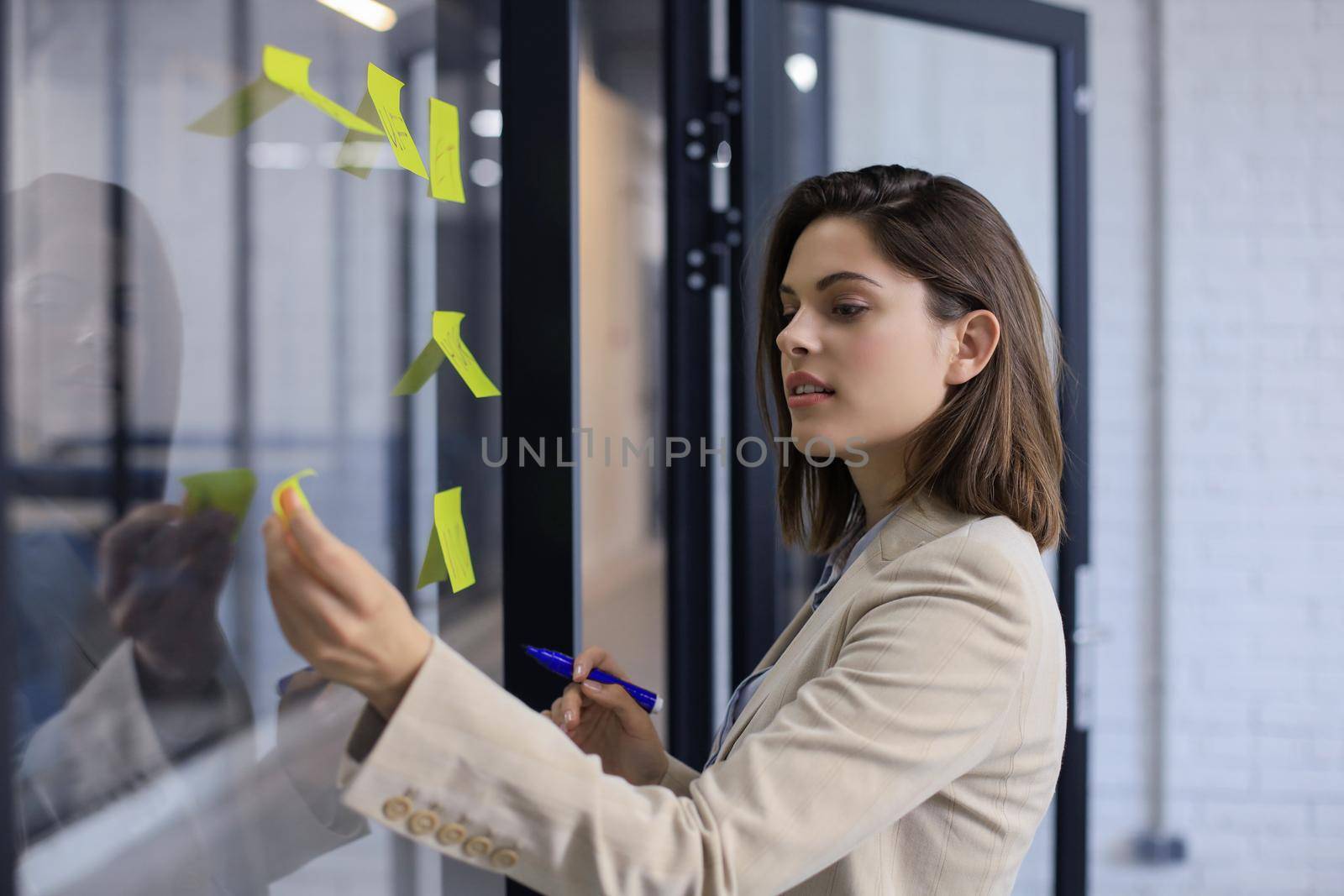 Attractive business woman post stickers on glass at office and writing on them. by tsyhun
