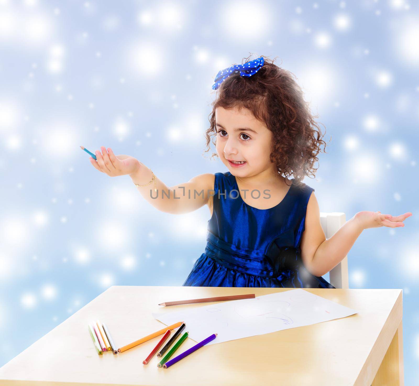Adorable little girl in a blue dress drawing pencils . Girl sitting at the table.Blue winter background with white snowflakes.