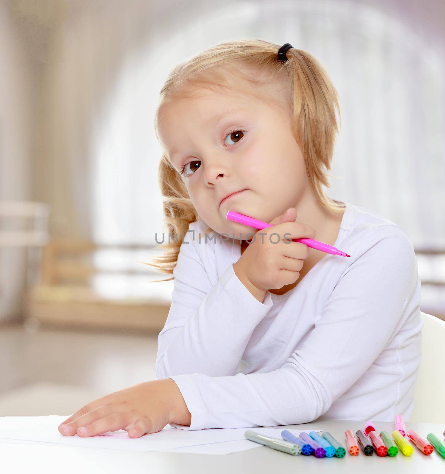 Pretty little blonde girl drawing with markers at the table.The girl thoughtfully looks into the camera.The concept of pre-school education of the child among their peers . in gaming room