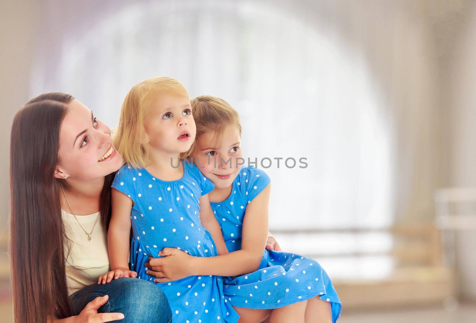 Beautiful young mother with her two daughters. All look up.On the background of the hall with large semi-circular window.