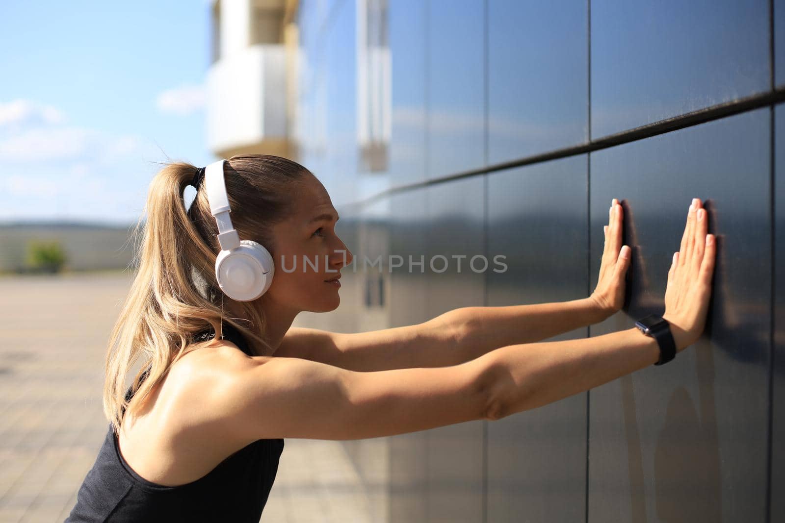 Attractive young fitness woman wearing sports clothing exercising outdoors, stretching exercises