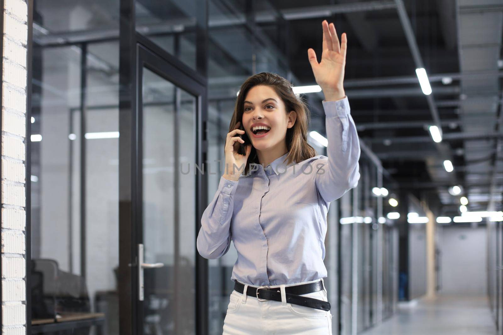 Attractive business woman talking by smartphone and waving hand by greeting you