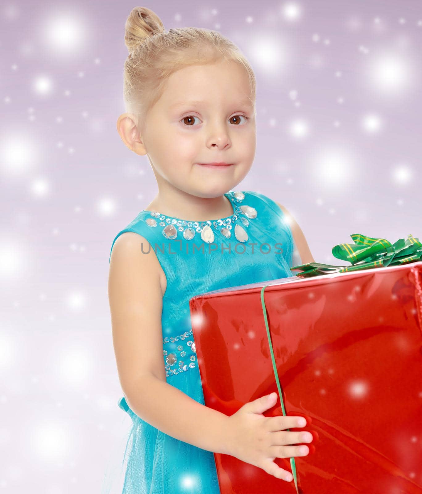 Caucasian little girl in a blue dress, holding the hands of the big red box that is a gift.The concept of celebrating the New year, Holy Christmas, or child's birthday on a purple background