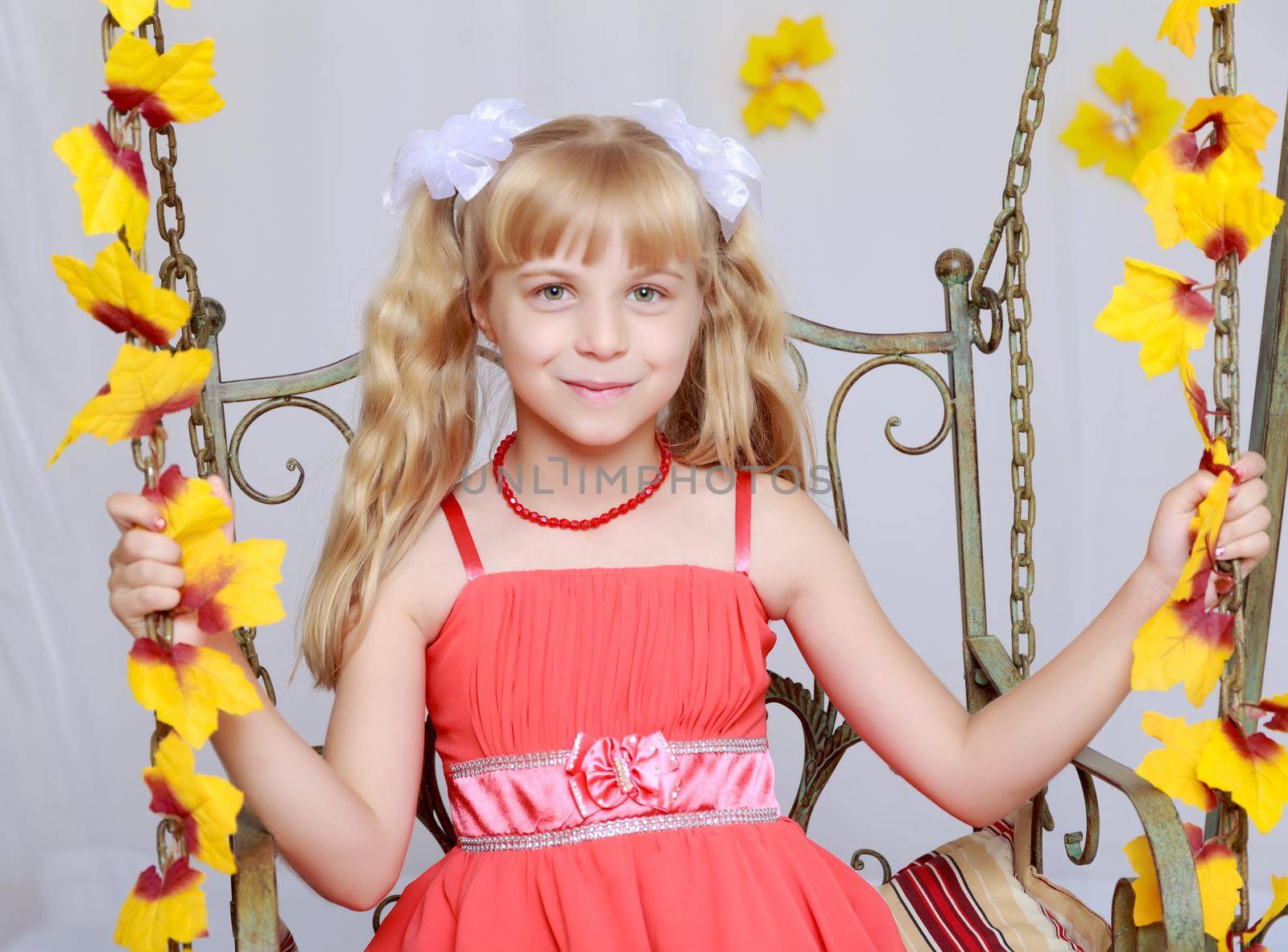 Cute little girl in red long dress on a swing decorated with yellow flowers. close-up