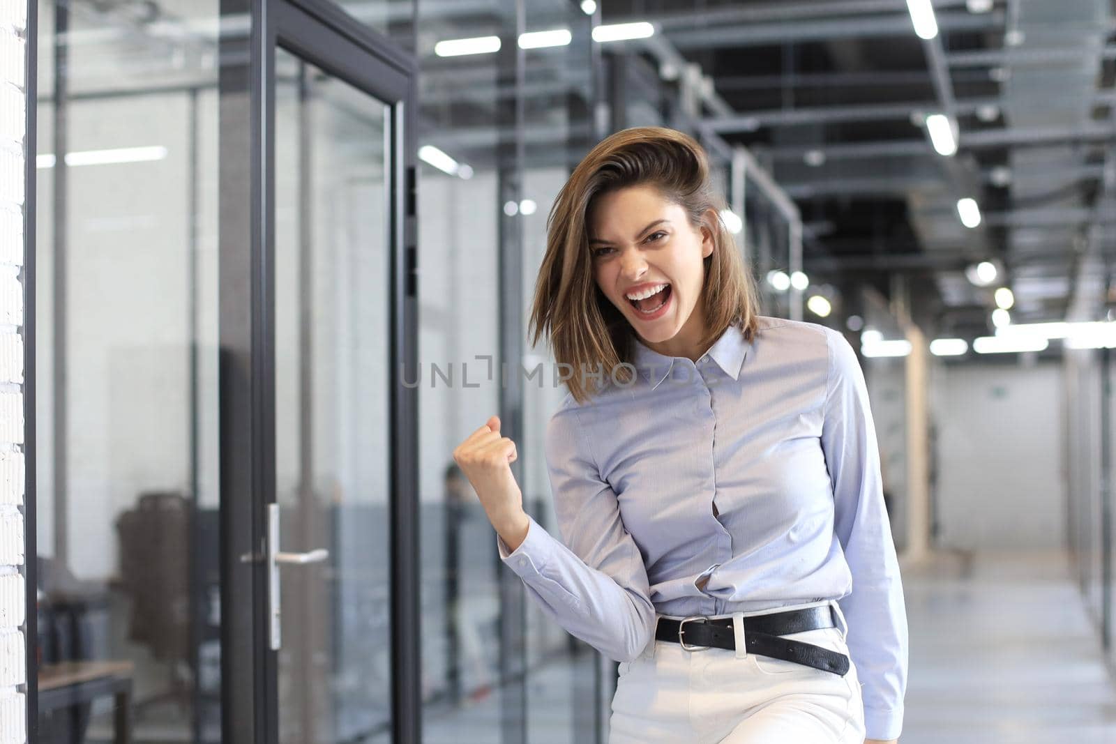 Beautiful businesswoman is keeping arm raised and expressing joyful in office