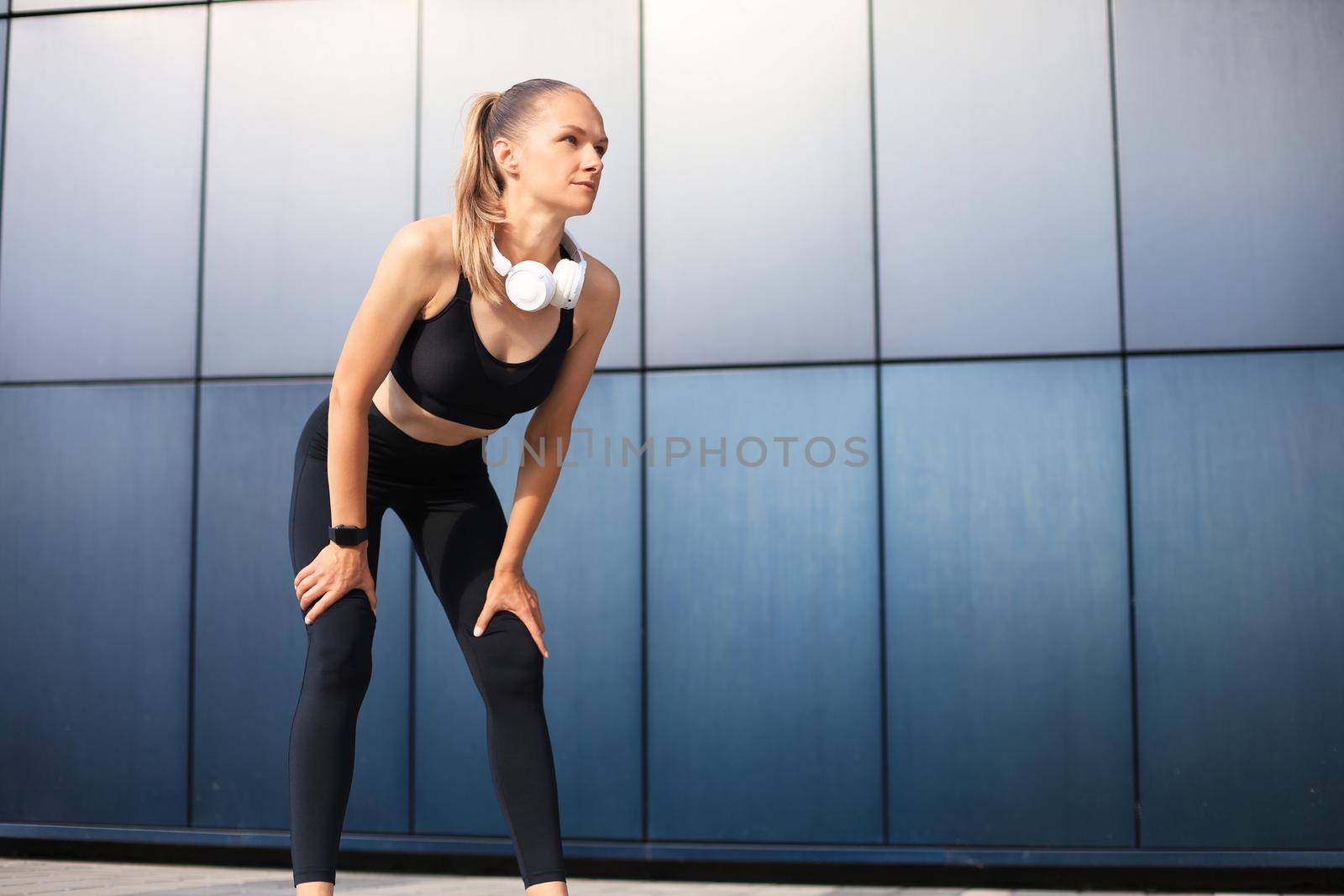 Young fitness attractive sporty girl resting after intensive evening run outdoor at sunset in city