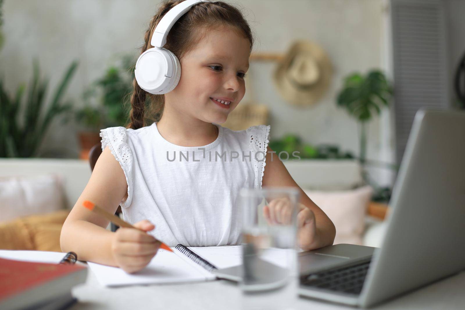 Distance learning. Cheerful little girl girl in headphones using laptop studying through online e-learning system