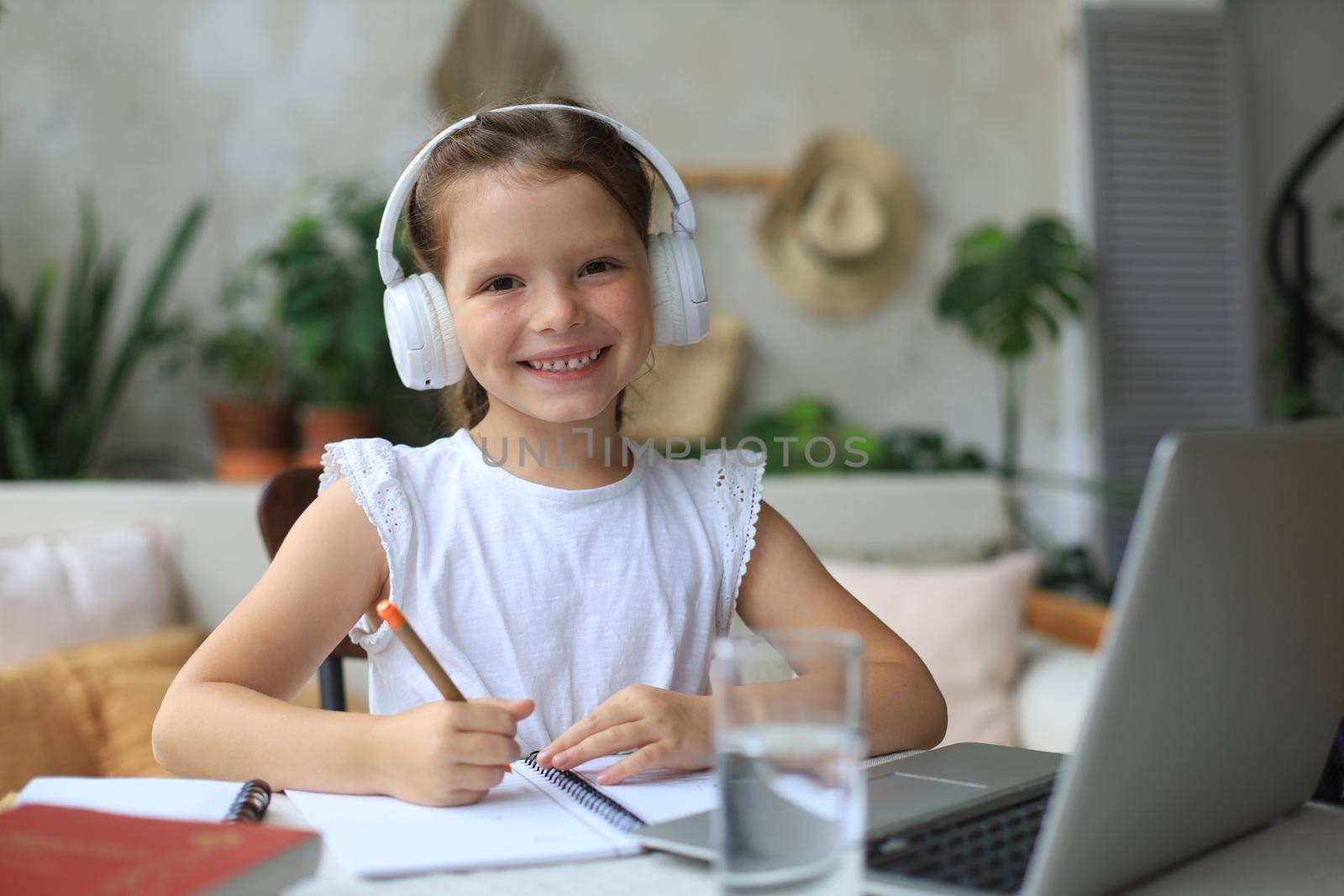 Smiling little girl in headphones handwrite study online using laptop at home, cute happy small child in earphones take Internet web lesson or class on PC. by tsyhun