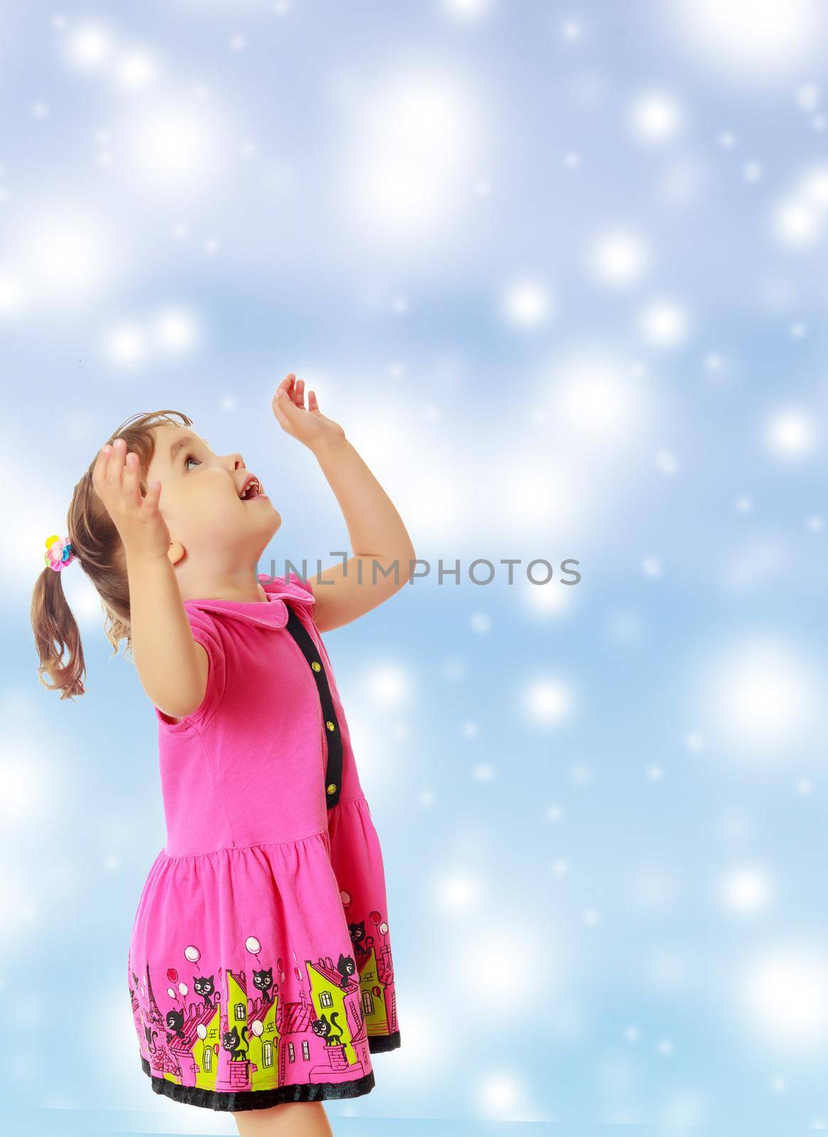 Cute little girl with pigtails on the head , in a pink dress. The girl was looking at the top turned sideways to the camera.On new year or Christmas blue background with white big stars.