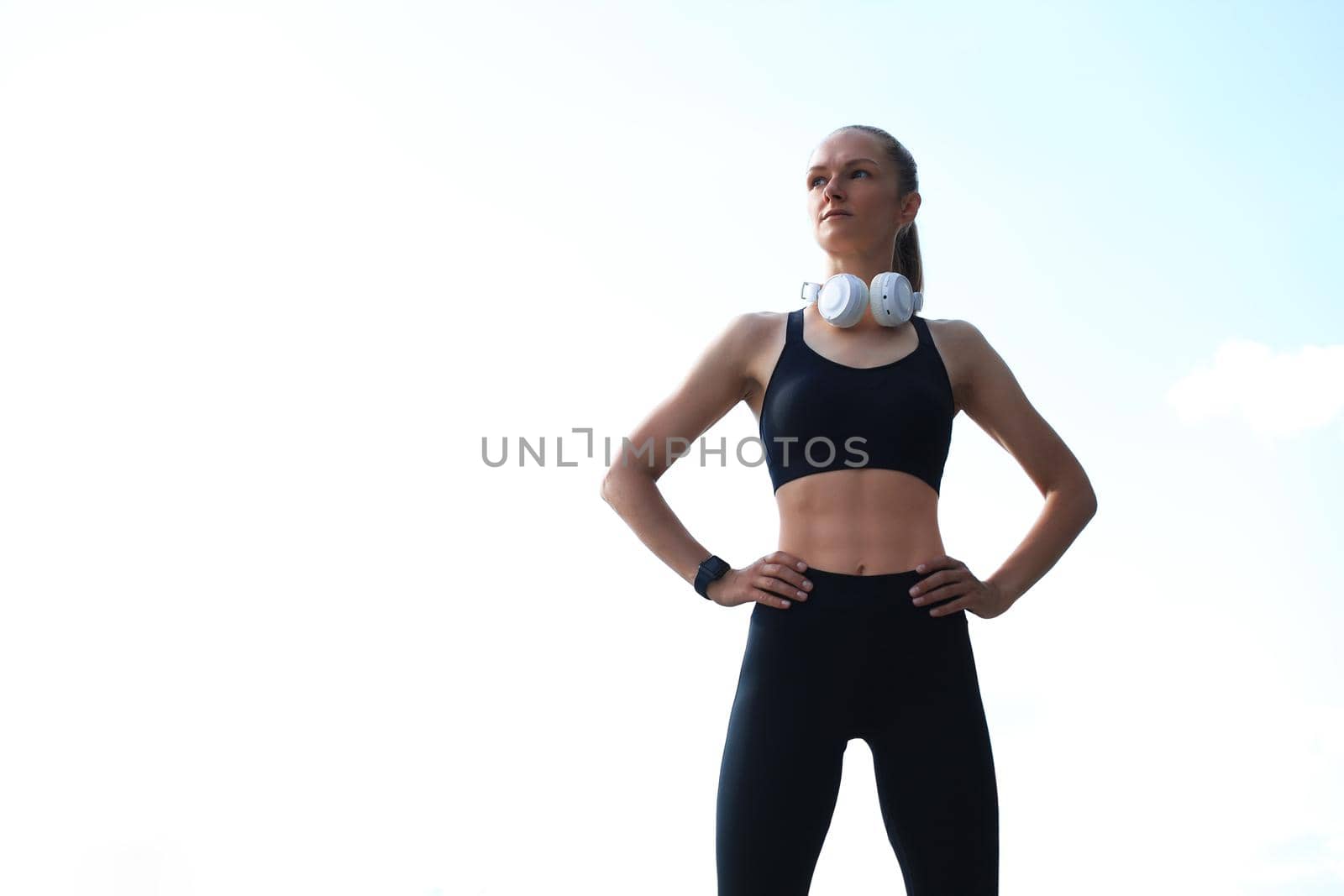 Beautiful woman in sports clothing and earphones looking aside from camera
