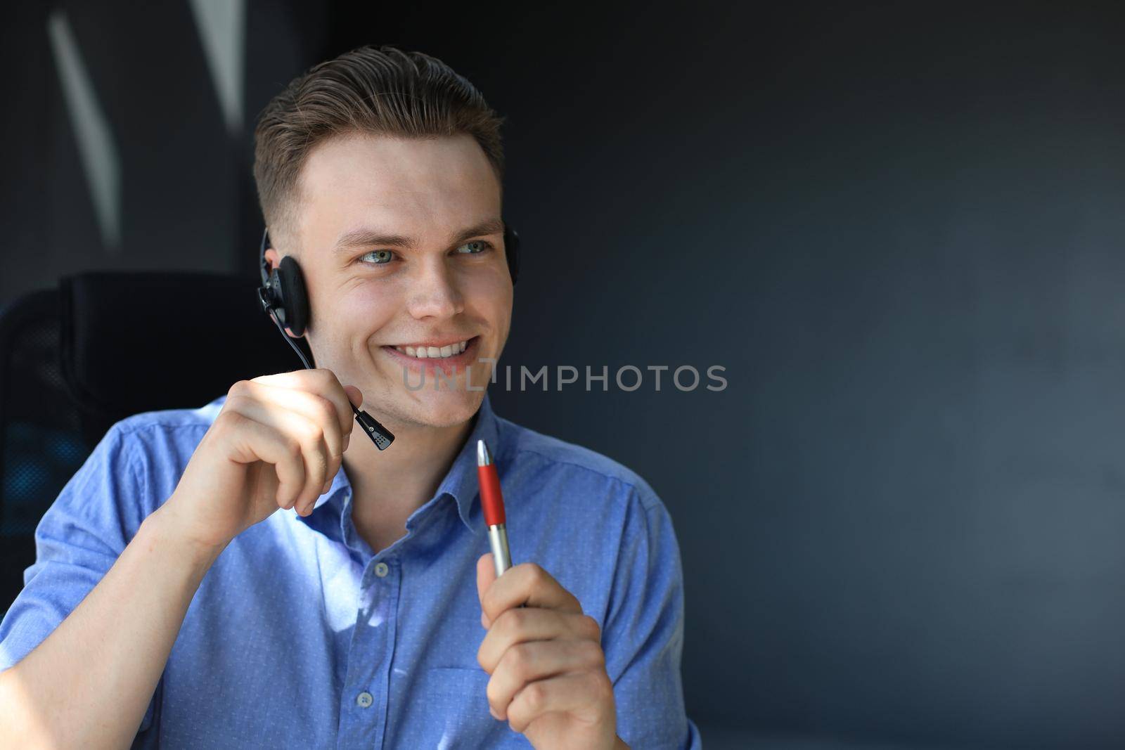 Cheerful young support phone male operator in headset, at workplace while using laptop, help service and client consulting call center concept. by tsyhun