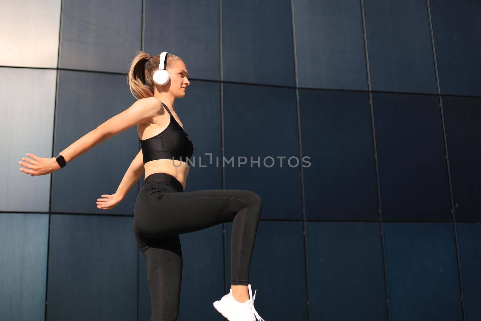 Photo of modern athletic woman in sports clothing jumping while exercising outdoors. by tsyhun