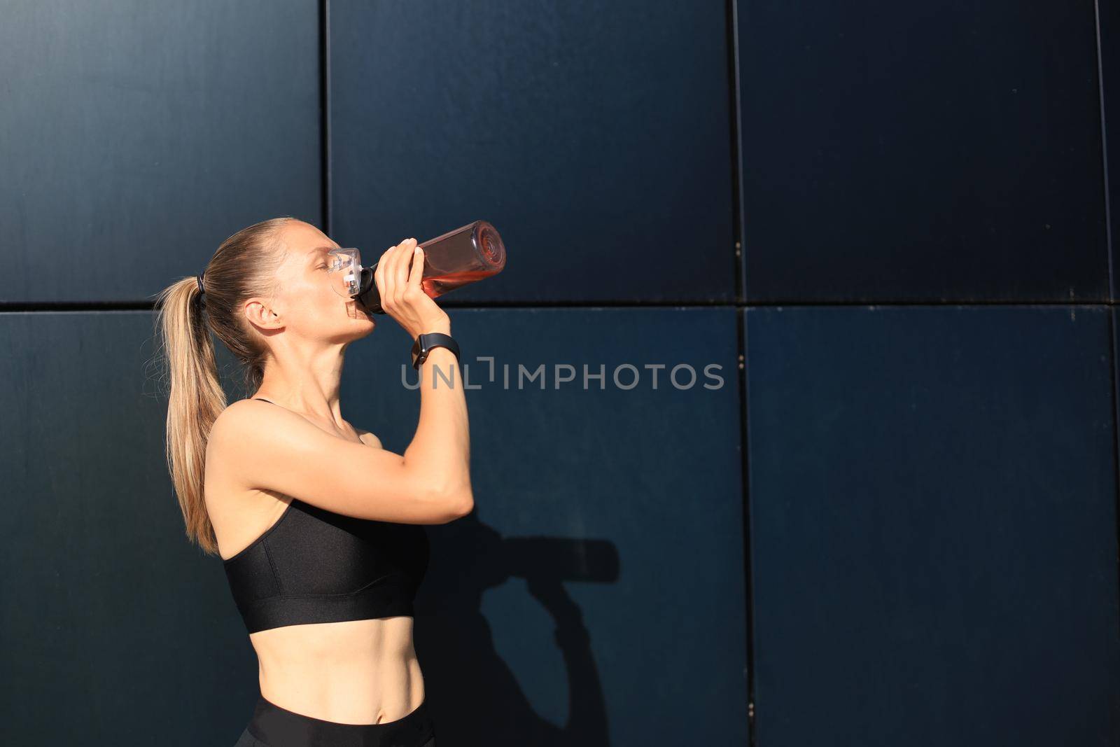 Close up of a young attractive tired sportswoman outdoors, drinking water from a bottle